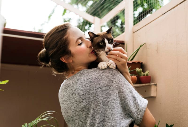 Woman cuddling calico cat in a conservatory