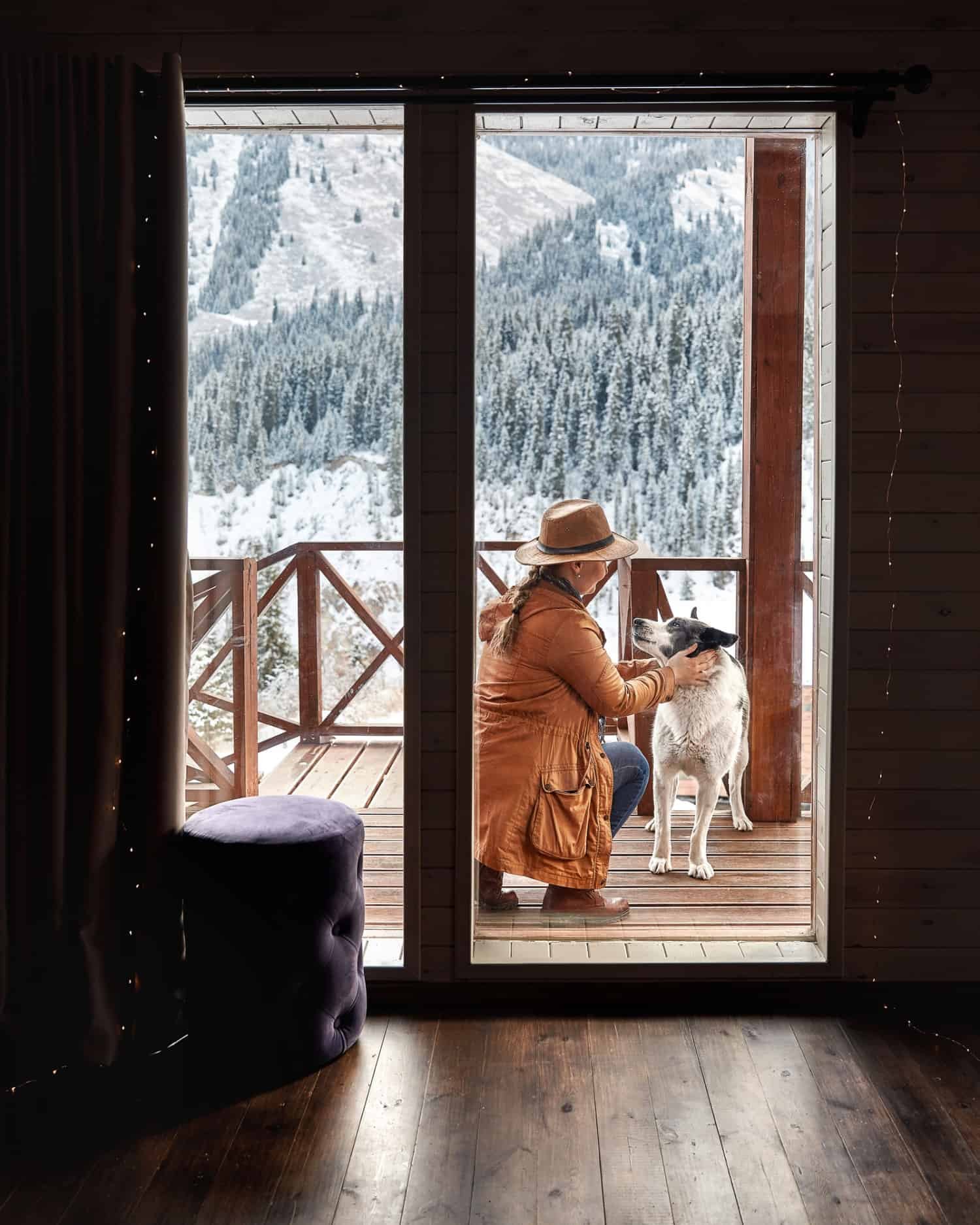Frau mit Hut spielt im Winter mit ihrem Hund auf dem Deck eines haustierfreundlichen Ferienobjekts